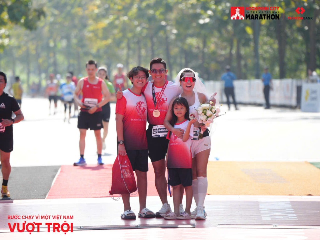 Cả gia đình Phạm Đức Anh tại vạch đích Marathon — vợ cầm hoa, hai con mặc đồng phục Diamond Runners